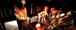Workers in special protective suits clamp crucible, pour molten glass